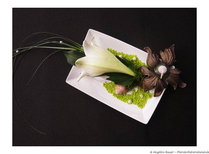 Eleganter Tischschmuck in weiß grün gehalten mit einer Lilie. Die Kerze steht in einer Blüte aus Gusseisen (von oben).